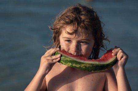 Téléchargez les photos : Portrait d'enfants d'été. Enfant avec fruits et jus de pastèque. Fruits d'été saisonniers. Enfant tenant tranche de pastèque rouge sur la plage. Vacances d'été amusantes. Enfant dégustant des fruits d'été, pastèque douce - en image libre de droit