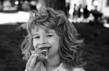 Photo for A boy with takes a bite of pizza. The child eat slice of pepperoni pizza. Funny kids face - Royalty Free Image