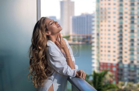Foto de Sexy woman on terrace. Young lady in stylish shirt poses on balcony and enjoys spring. Girl on terraced house by the sea, enjoy morning fresh air with ocean. Sensual woman enjoy town view at terrace - Imagen libre de derechos