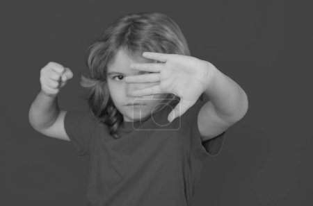 Foto de Niño en camiseta roja haciendo gesto de parada en el fondo del estudio aislado. Muchacho mostrando símbolo de advertencia, señal de mano no. Concepto de protección, intimidación, abuso y violencia infantil - Imagen libre de derechos