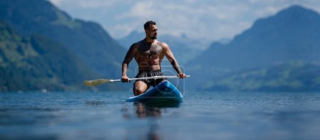 Photo for Male fit strong muscular model with paddle board. Guy paddling on paddleboard. Healthy summer lifestyle. Water sport. SUP surfing in summer vacation in Alps lake in Switzerland - Royalty Free Image