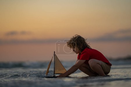 Photo for Childhood concept. Kid boy holding tou boat. Cute little blond boy put toy boat in the sea water waves at the beach on summer vacation. Happy child playing with ship. Summer sea dream and imagination - Royalty Free Image