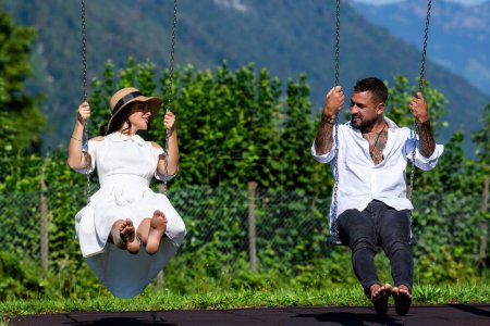 Man and woman sitting together on swing and enjoying summer. Couple lovers enjoy honeymoon and summer vacation on green nature. Couple in love siiting on the swing and relax. Valentines day
