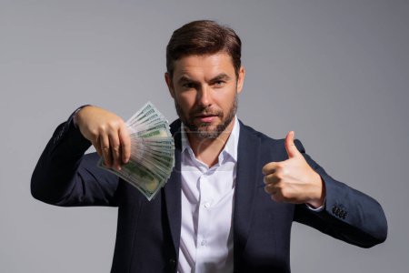 Business man hold money on gray studio isolated background. Rich man in suit with money dollar bills. Successful businessman with dollar banknotes. Rich millionaire in suit holding money