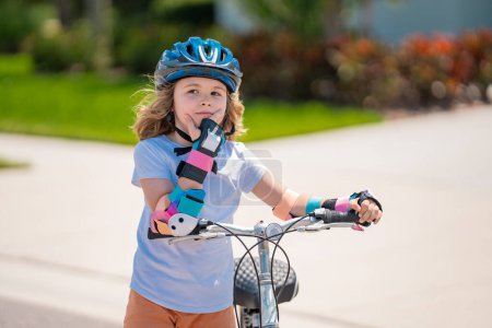 Enfant en vélo dans un parc d'été. Les enfants apprennent à conduire un vélo sur une allée à l'extérieur. Enfant à vélo dans la ville portant des casques comme équipement de protection. Enfant à vélo, vélo en plein air