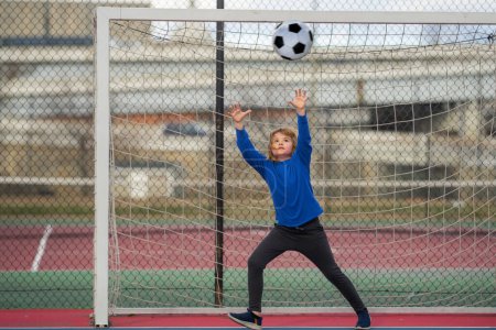Kid Goalkeeper catches football ball during a football game. Football moment with kids. Child boy goalkeeper catch soccer ball. Kid goalkeeper with a soccer ball. Goalkeeper training football