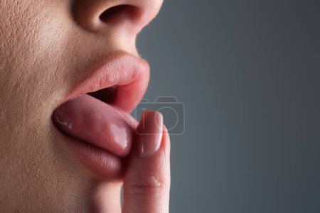 Nägel-Maniküre. Zunge raus und Finger lecken. Großaufnahme der herausstreckenden weiblichen Zunge. Makrozunge lecken Finger. Großaufnahme des Mundes der Frau mit der Zunge. Sexy Zungen. Sinnlicher Fingerlecken