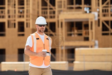 Photo for Builder in helmet on coffee break at construction site american wood frame house construction. Worker in helmet on the new building. Builder with hardhat helmet on construction site - Royalty Free Image