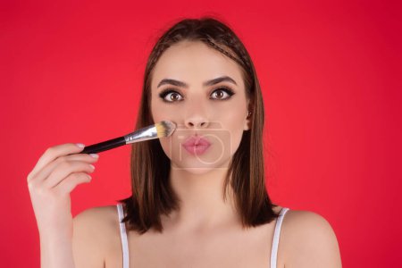 Beautiful woman applying makeup holding brush. Beauty make up concept of an young woman. Beauty salon. Skin care and natural makeup. Girl gets blush on the cheekbones. Beauty care and treatment