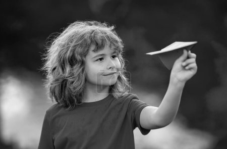 Foto de Niño divertido sueña con convertirse en un aviador jugando avión de papel al aire libre. Concepto de niños en crecimiento. Niño feliz jugando con avión de papel en el jardín de verano. Un chico tirando aviones de papel en el parque. Infancia - Imagen libre de derechos
