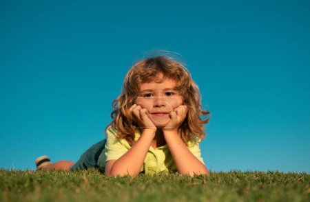 Téléchargez les photos : Portraits d'enfants heureux jouant et se reposant sur l'herbe à l'extérieur dans le parc d'été. drôle enfant visage extérieur - en image libre de droit