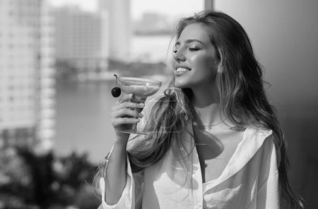 Téléchargez les photos : Femme sensuelle profiter de boire coctail sur la terrasse balcon pendant les vacances d'été. Femme élégante buvant un cocktail alcoolisé à la maison. Belle fille boire un cocktail - en image libre de droit
