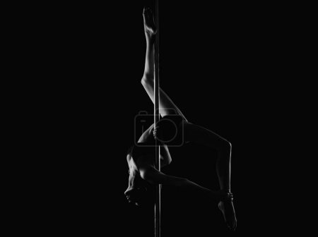 Téléchargez les photos : Flexible fille fait des exercices de gymnastique sur le pylône pour l'étirement. Belle femme flexible sexy démontre sexy corps flexible. Flexibilité tendue sur le noir. Corps féminin flexible. Danse du pôle - en image libre de droit