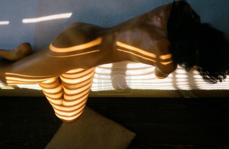 Foto de Un cuerpo de mujer sensual por la mañana. Sexy hembra en la cama con sombras matutinas. Cuerpo desnudo perfecto de dama sexy. Hermosa espalda femenina y culo - Imagen libre de derechos