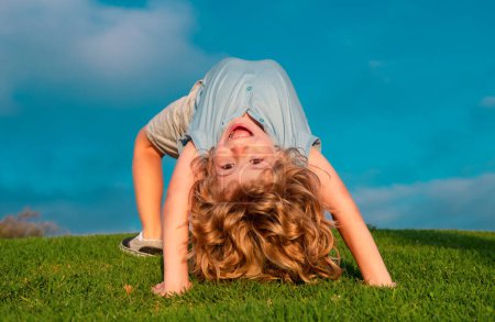 Foto de Divertido niño lindo haciendo ejercicio divertido. Niño feliz jugando en la hierba verde al aire libre en el parque de primavera - Imagen libre de derechos