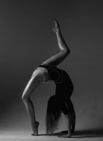 Foto de Chica flexible bailando. Hermoso cuerpo de mujer flexible. Retrato de estudio de arte de moda de la mujer flexible en forma sexy en negro. Gimnasia mujer bailarina delgada y flexible realizando. Estiramientos ejercicio - Imagen libre de derechos