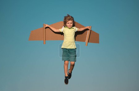 Photo for Kids fly. Funny child boy pilot flying with toy cardboard airplane wings on blue sky, copy space. Start up freedom concept, carefree kid - Royalty Free Image