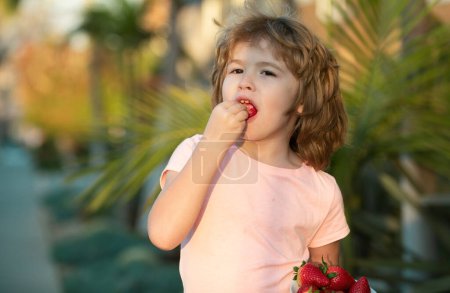 Un niño sosteniendo una fresa. Lindo bebé con fresa, al aire libre