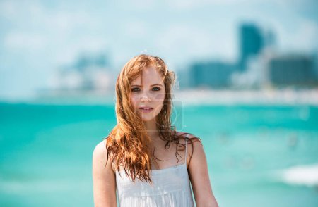 Photo for Sunner portrait of redhead beautiful girl at beach. Young tanned woman enjoying breeze at seaside. Carefree woman smiling with sea ocean in background - Royalty Free Image