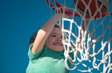 Foto de Lindo chico sonriente juega baloncesto y haciendo slam dunk. Retrato de primer plano del jugador de baloncesto niño niño - Imagen libre de derechos
