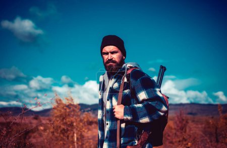 Foto de Hunter con escopeta a la caza. Hombre cazador barbudo sosteniendo arma y caminando en el bosque. Otoño - Imagen libre de derechos