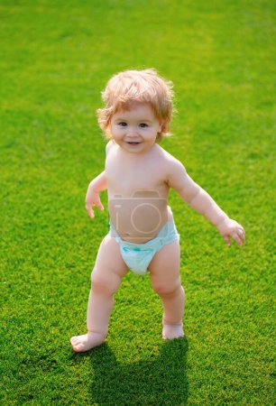 Téléchargez les photos : Portrait de mignon petit enfant caucasien s'amusant dans le jardin. Petit enfant rampant sur la pelouse d'herbe verte pendant la promenade dans la cour. Bonne enfance et santé bébé - en image libre de droit