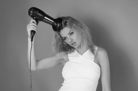 Photo for Blonde woman with hair dryer on studio background. Hairs style and beauty concept. Beautiful girl with hairdryer drying hair. Beauty model dries hair with hair dryer. Blow dryer - Royalty Free Image
