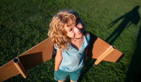 Foto de Lindo niño jugando con alas de avión de juguete en el parque de verano. Innovación tecnológica y concepto de éxito. Kid piloto divertirse en la hierba en el parque - Imagen libre de derechos