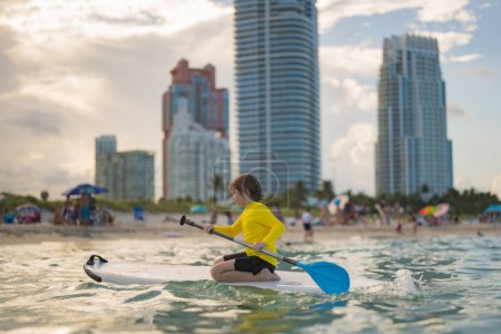 Summer vacation with kids in Miami beach. Kid and Summer sea. Child boy paddling on paddle board or sup. Summer lifestyle. Summer Water sport. Kid Boy swimming with paddle board