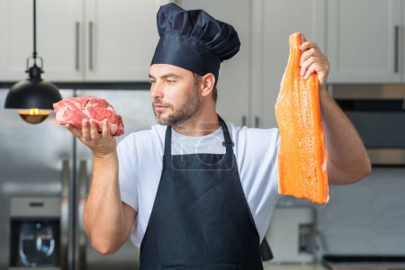 Photo for Handsome man cooking fish and meat, salmon and beef in kitchen. Portrait of casual man cooking in the kitchen with fish and meat ingredients. Casual man preparing raw fish and meat in kitchen - Royalty Free Image