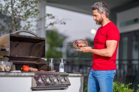 Le barbecue. Homme préparant barbecue grill extérieur. Homme cuisiner des aliments savoureux sur barbecue grill à l'arrière-cour. Chef préparant la nourriture sur barbecue. Homme millénaire griller de la viande sur le gril. Bbq. Grillades de repas