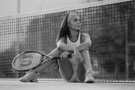 Téléchargez les photos : Modèle sport chaud. Joueuses de tennis assises sur un court de tennis près de la raquette et du ballon. Belle fille sexy posant sur le court de tennis. Sexy fille de tennis. Portrait de belle femme posant sur la cour - en image libre de droit