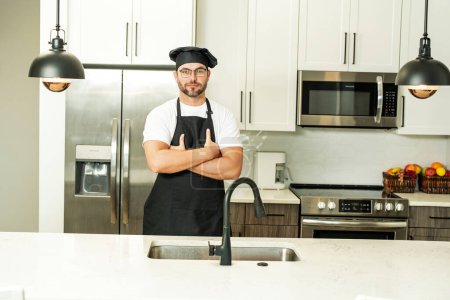 Handsome man chef in uniform cooking in the kitchen. Restaurant menu concept. Hispanic man in baker uniform. Cooking and culinary. Male chef in working uniform, black apron, chef hat