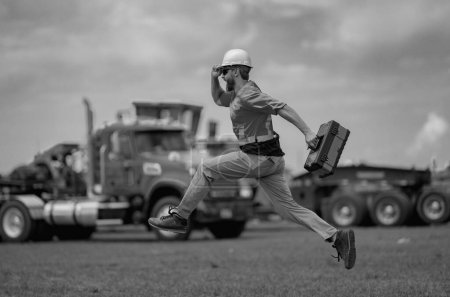 Photo for Hispanic 40 s builder excited jump on site construction. Excited builder construction worker in a safety helmet jumping in front of the trucks. Excited crazy builder man in helmet jump outdoor - Royalty Free Image
