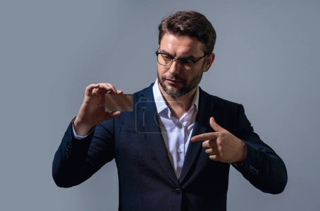 Credit card. Caucasian millennial successful 40s business man holding banking card isolated on gray background, studio portrait. People lifestyle concept. Purchasing and cashback rewards