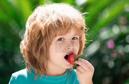 Nourriture saine pour enfants. Adorable gosse mangeant de la fraise sur fond de printemps vert. Gros plan enfants heureux visage