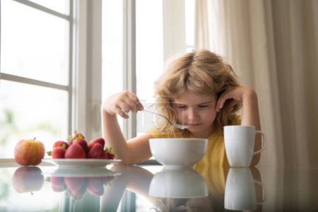Unhappy little boy child sit at table at home kitchen have no appetite for healthy breakfast. Upset kid refuse to eat cereals with milk. Adorable sad tired kid eating low fat soy milk in bowl cereal