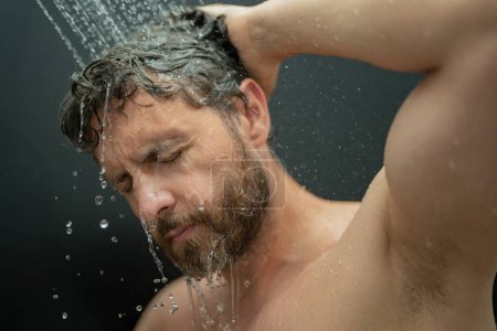 Un hombre duchándose. Hombre lavar el cabello con champú bajo el agua que cae de la cabeza de la ducha. Un tipo de rutina matutino duchándose. Cuidado corporal higiene ducha. El hombre está bajo las gotas de agua en la ducha. Bienestar y spa