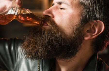 Swag guy with alcohol close up partrait. Drunk man. Bearded man drinking whiskey, brandy or cognac. Pub retro vintage interior. Hipster barman concept