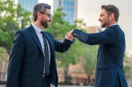 Business man shaking hands, giving fist bump. Two businessmen giving fist bump outdoor, friendly team, have positive expressions, demonstrate agreement