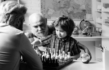 Grandfather father and son playing chess, happy men generations family. Granddad and cute little boy grandson study and learn together. Senior grandpa and middle aged dad play with grandchild son