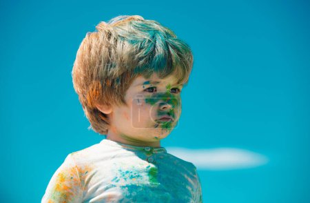 Kinderholi-Fest. Gemaltes Gesicht eines lustigen Kindes. Kleiner Junge spielt mit Farben