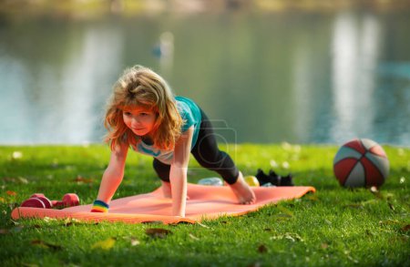Photo for Child is pushing up on the green meadow, working out wearing sportswear, t-shirt outdoor. Kids doing push up outdoor. Gymnastic for children. Kid pushing up - Royalty Free Image
