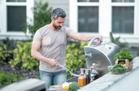 Hispanic man cooking on barbecue in the backyard. Chef preparing barbecue. Barbecue chef master. Handsome man preparing barbecue, bbq meat. Grill and barbeque