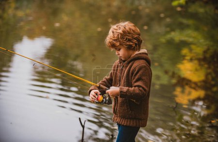 Téléchargez les photos : Petit pêcheur. Enfant garçon pêche en salopette à partir d'un quai sur le lac ou l'étang - en image libre de droit