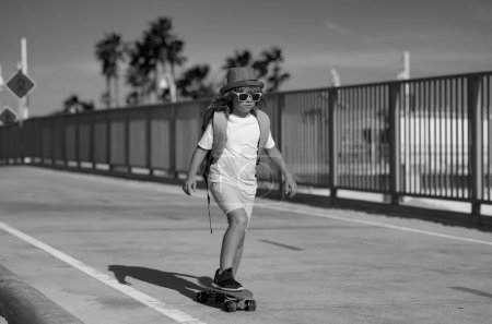 Foto de Niño montando monopatín en la carretera. Kid practicando skate. Los niños aprenden a andar en monopatín en un parque el soleado día de verano. Niño en patineta patinaje - Imagen libre de derechos