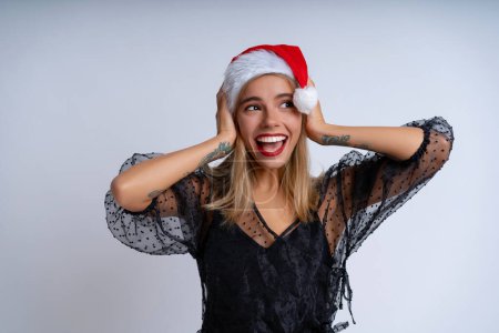 Téléchargez les photos : Capturée sur fond blanc, une jeune femme portant un chapeau de Noël et une élégante robe de soirée noire dégage une humeur festive et festive - en image libre de droit