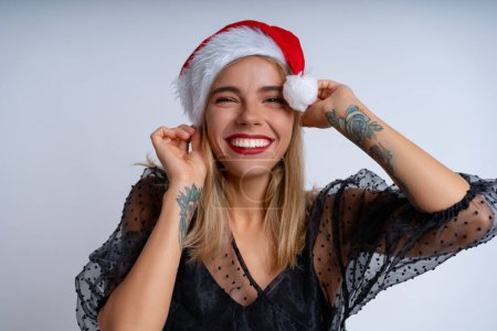 Photo for Against a white backdrop, a young woman wearing a Christmas hat and an elegant black evening dress, showcases a joyful and celebratory mood with a beaming smile - Royalty Free Image