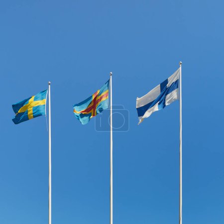 National flag of Sweden, Aland flag, national flag of Finland against the blue sky.