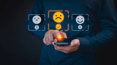Photo for Engaging in an online customer feedback survey, a user utilizes their mobile phone to display an angry emoticon on a virtual screen, sharing their opinion and reviewing service satisfaction. - Royalty Free Image
